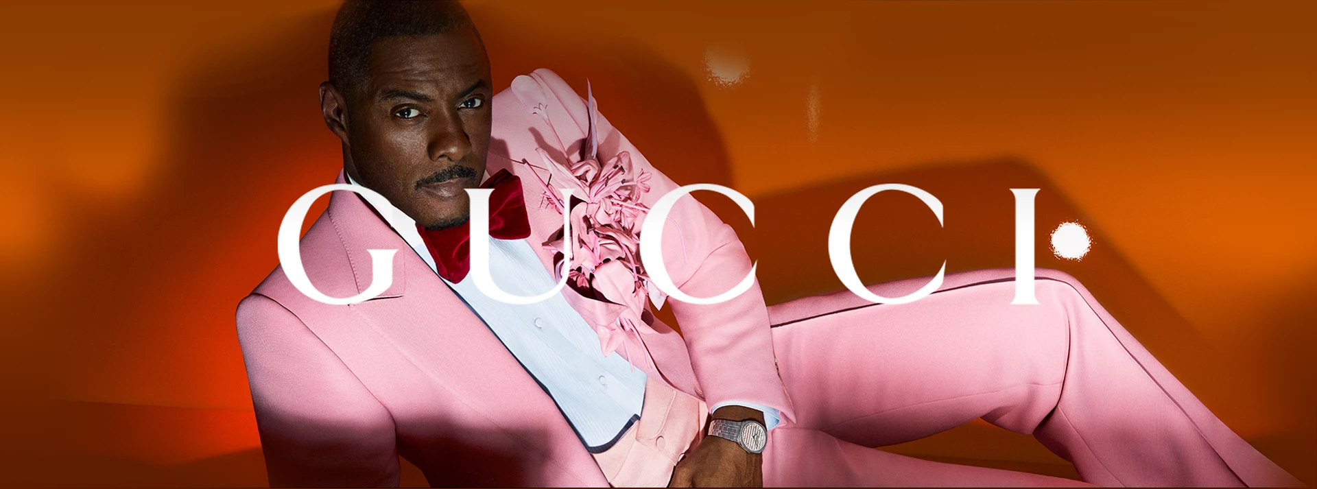 Idris Elba in pink suit on orange background