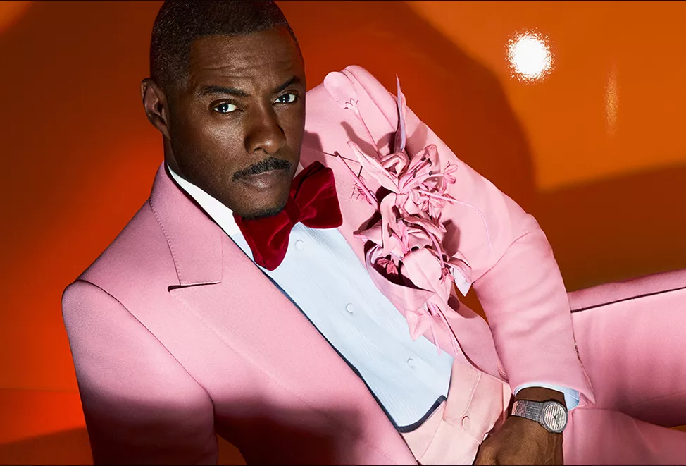 Idris Elba in pink suit on orange background